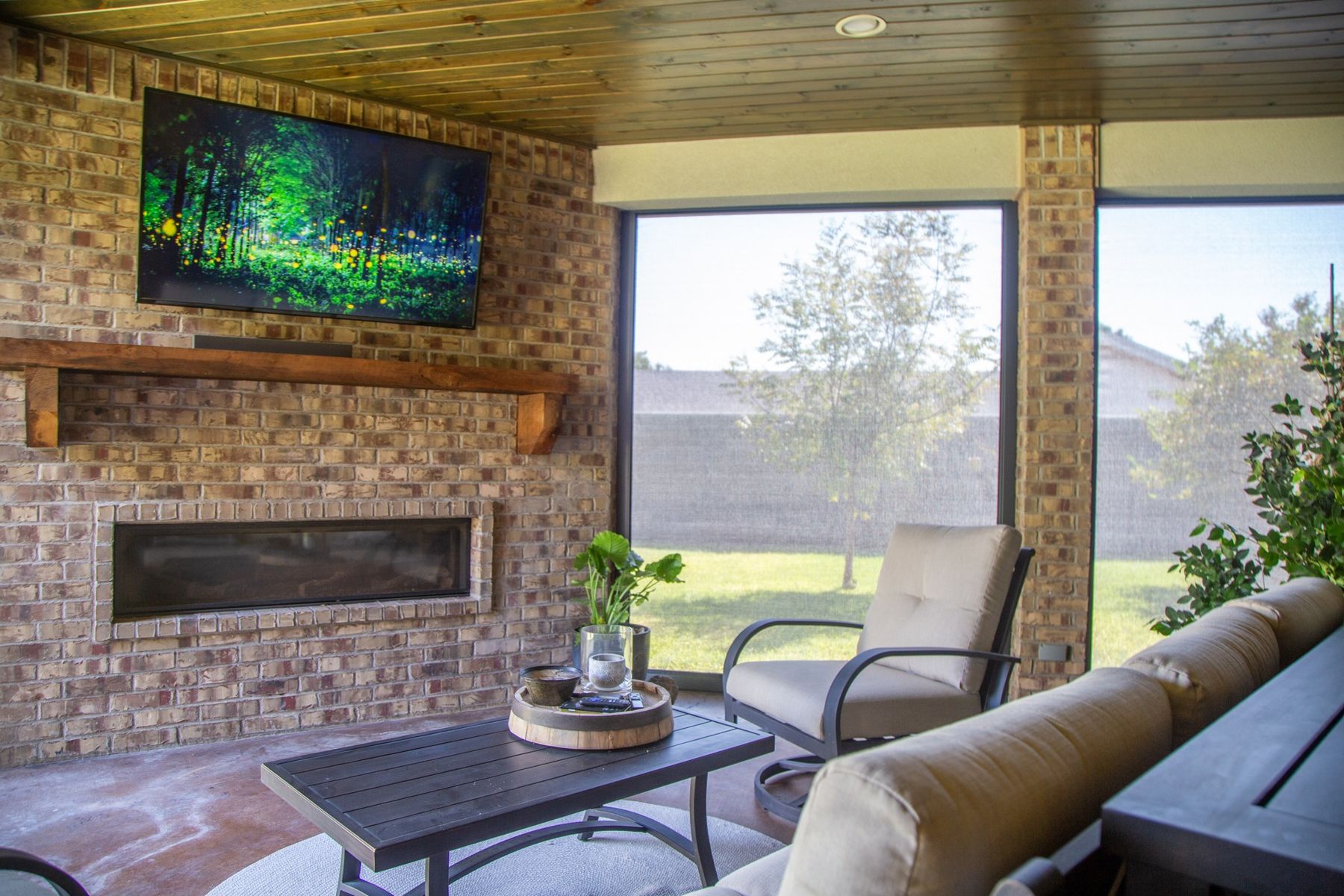 Screened patio with a fireplace, TV, and seating, looking out through lowered MagnaTrack screens